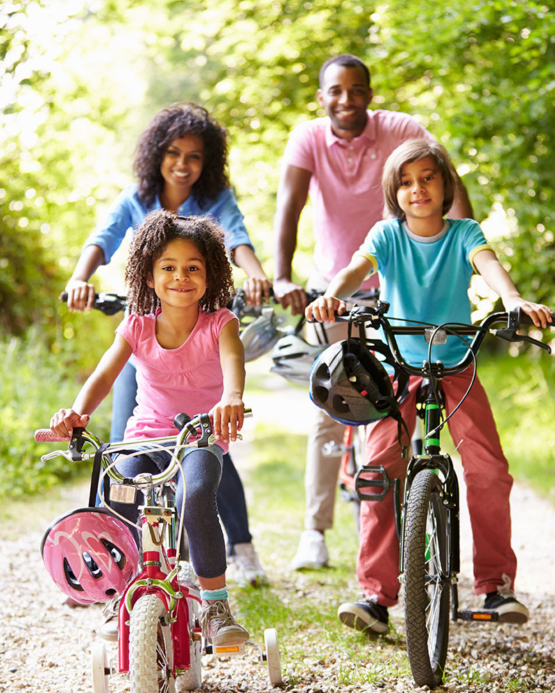 smiling family out riding bikes on a wooded trail 